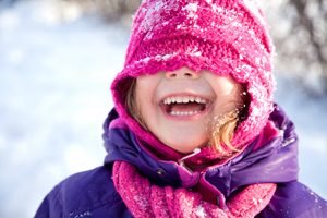 lachendes Mädchen mit rosa Mütze über den Augen im Schnee