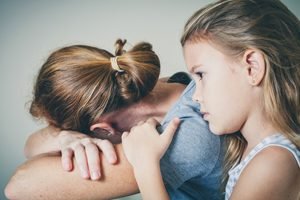 kleines Mädchen umarmt Mutter, die mit abgewandtem Gesicht weint