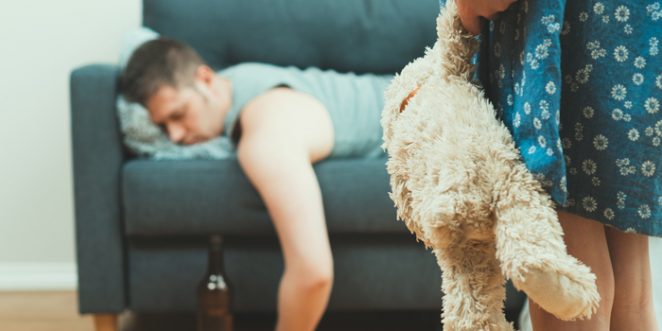 betrunkener Vater schlaeft auf Sofa, Kind steht mit Teddy davor