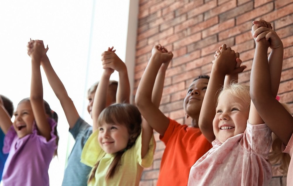 eine gruppe von kleinen kindern reisst die arme in die luft