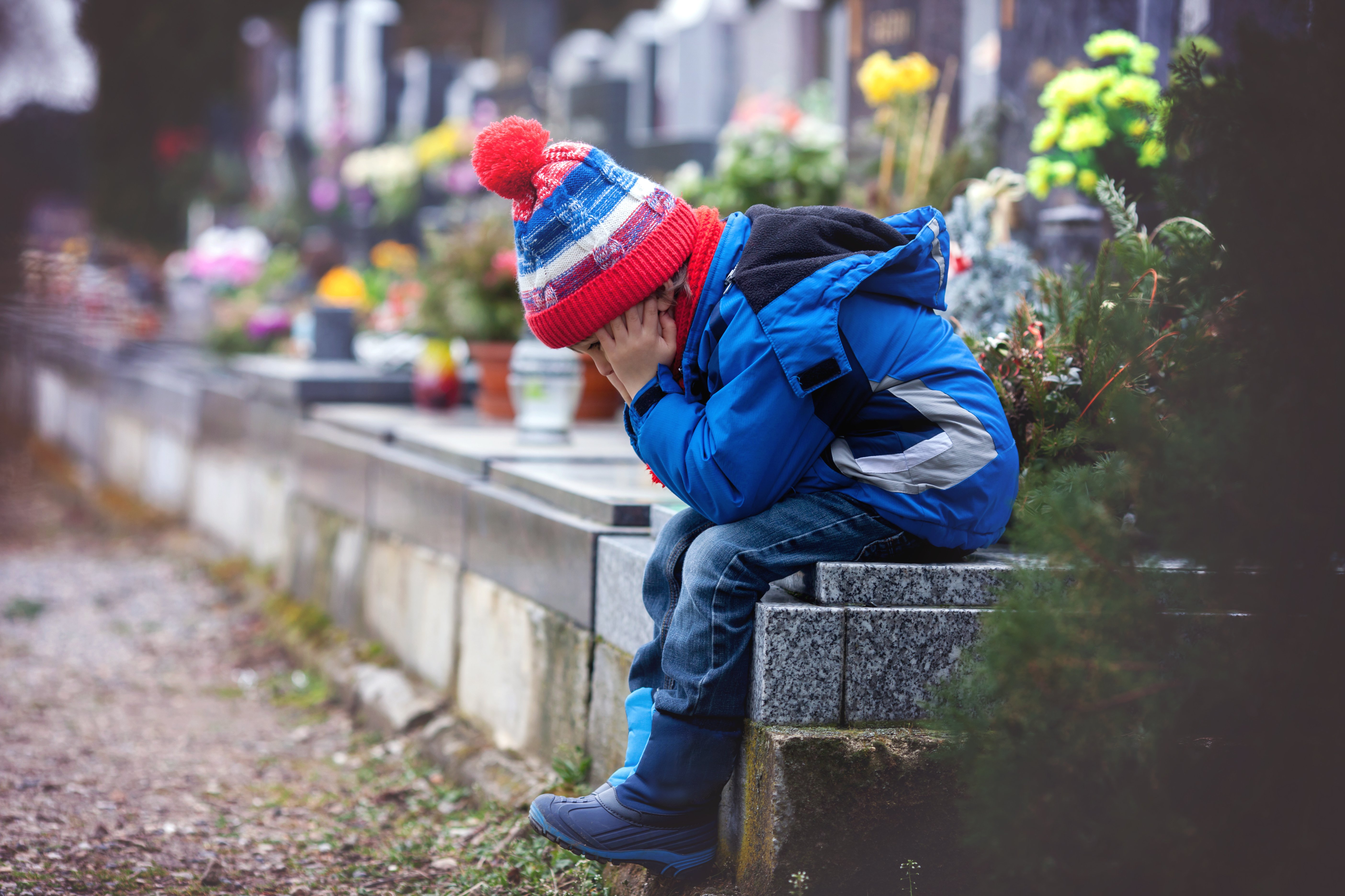 kleiner Junge sitzt traurig auf einem Friedhof