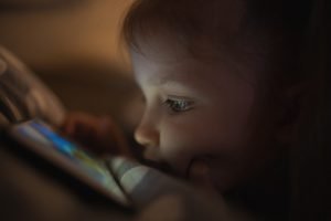 ein kind liegt mit einem smartphone unter der bettdecke