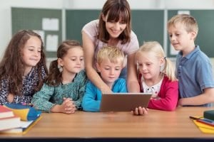 Lehrerin zeigt kleinen Kindern etwas am Tablet