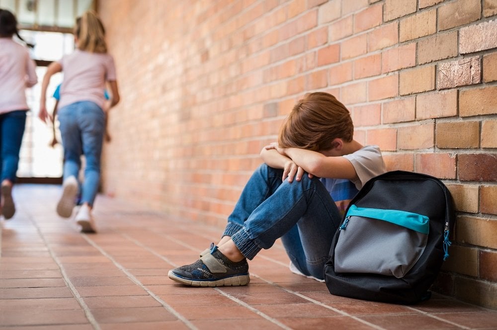 trauriger junge sitzt am boden in der schule