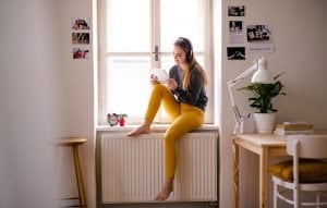 maedchen mit kopfhoerern und tablet auf der fensterbank