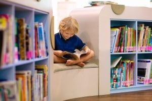 junge liest buch zwischen bücherregalen