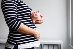 Schwangere Frau mit Sparschwein in der Hand. 