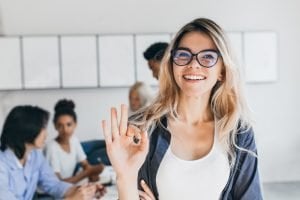 Frau lächelt, während andere Menschen im Hintergrund arbeiten