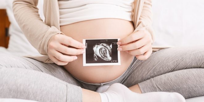 frau hält ultraschallbild vor babybauch